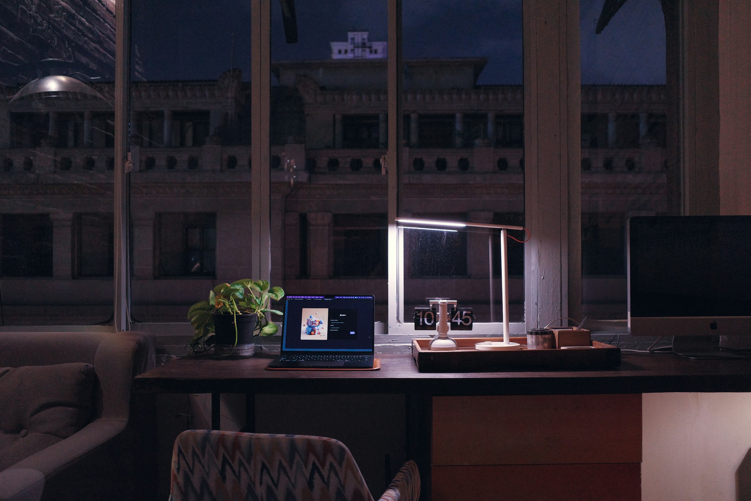 A warm desk at night with a laptop, lamp, and papers.